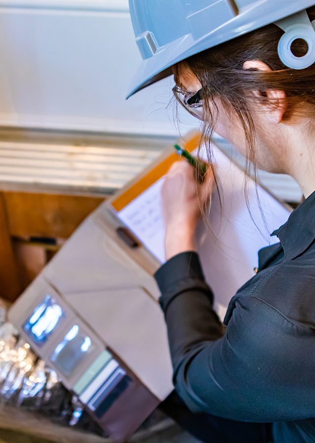 selective focus rear view of inspector woman taking notes, with unfinished aeration conduct isolated in aluminum and rock wool in the background.